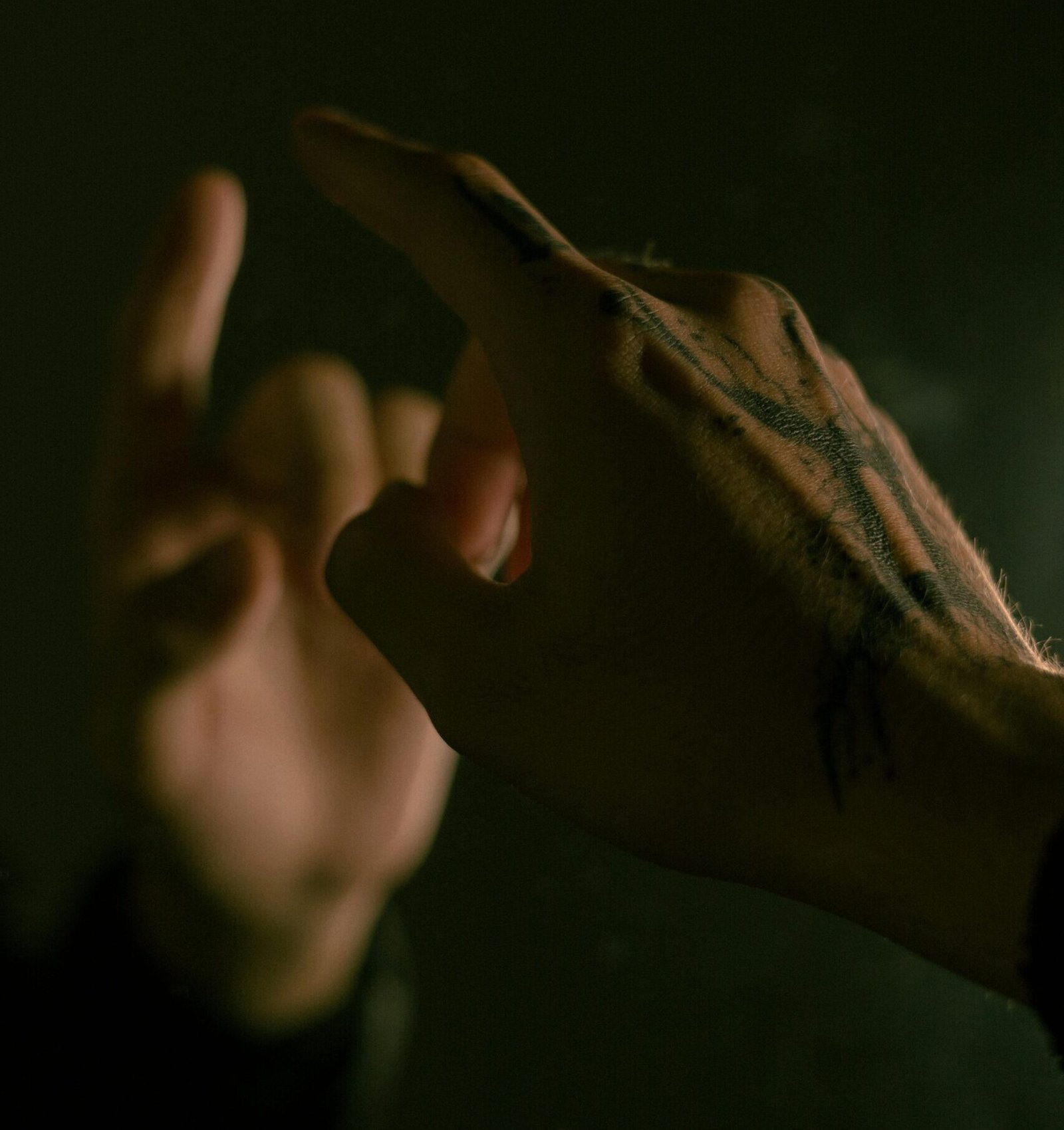 Close-up of tattooed hands pointing in dramatic, low light setting, capturing intricate details and shadows.